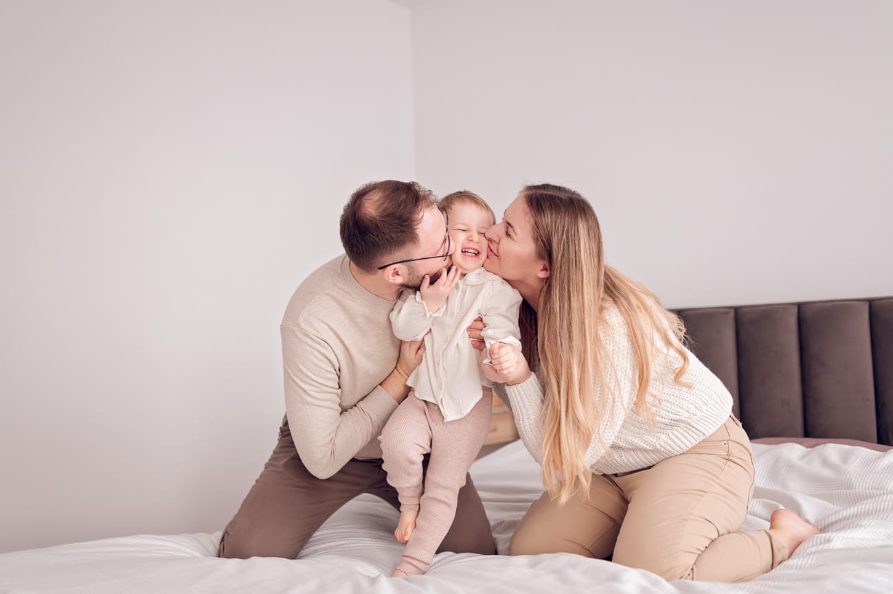 Rodzice całują córkę w sypialni sesja w domu
