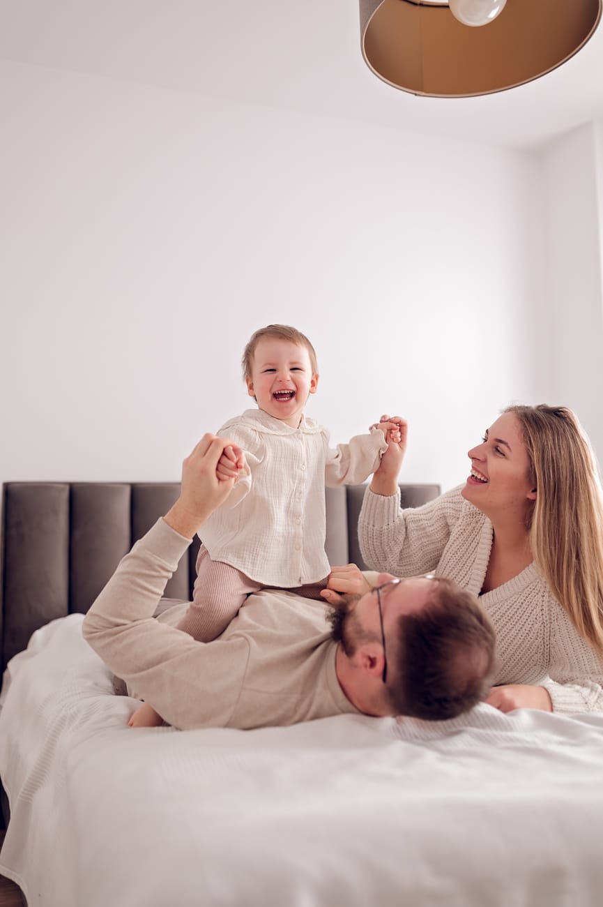 Dziewczynka radośnie bawiąca się z rodzicami w sypialni w domowym zaciszu.