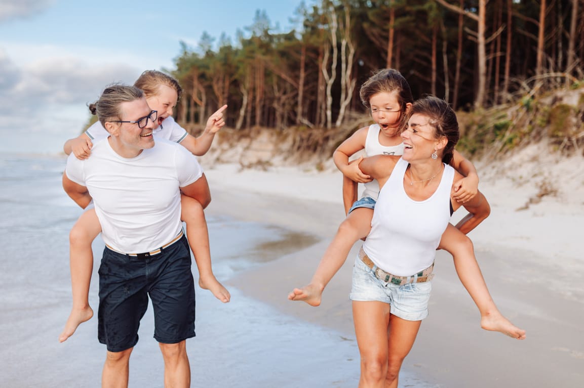 Siedmioletnie bliźnięta siedzące rodzicom na barana, radośnie wygłupiające się podczas sesji dziecięcej w Gdyni
