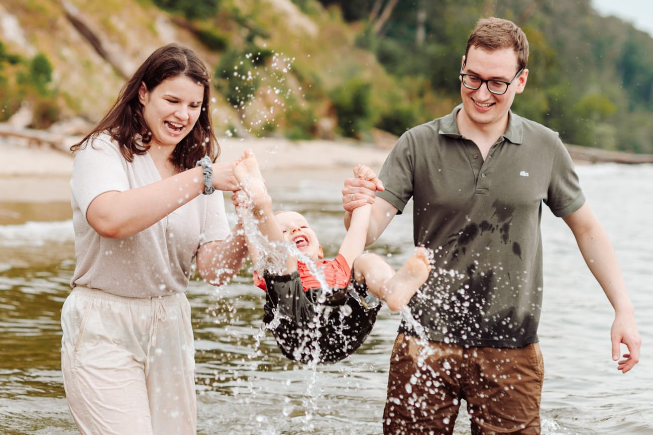 Rodzice huśtający roześmianego synka w morzu podczas sesji dziecięcej w Gdyni