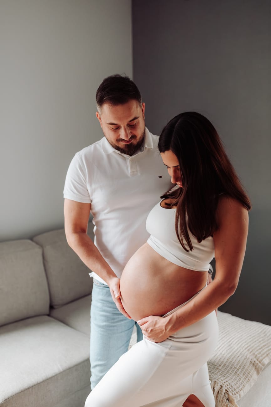 Para przytulona w salonie patrzy na brzuszek ciążowy sesja ciążowa Gdynia
