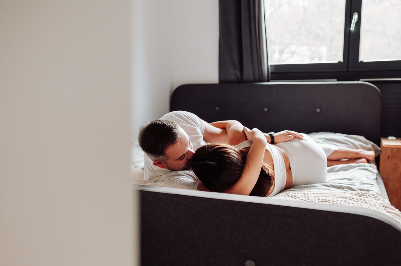 Domowa sesja ciążowa  i młoda para przytulająca się w sypialni