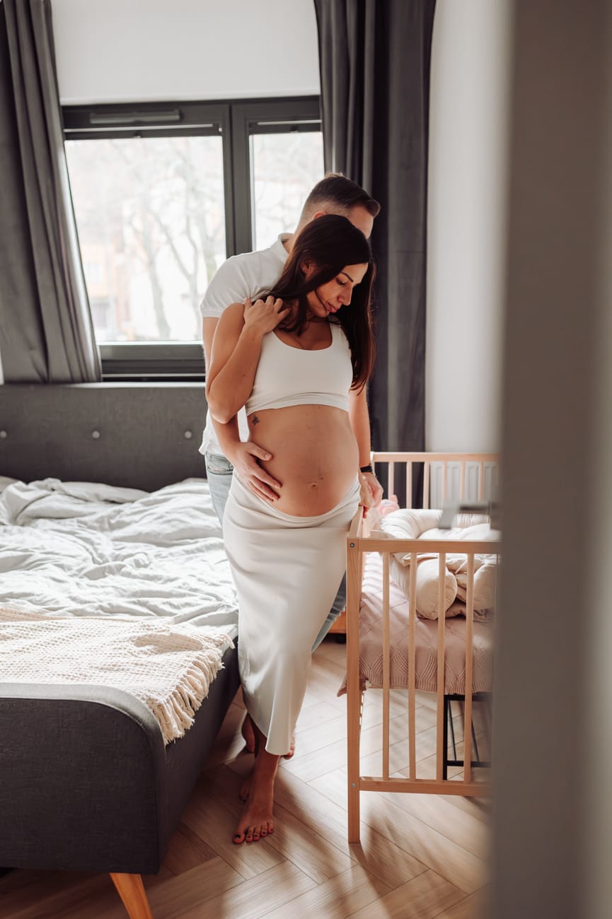 Para patrzy na łóżeczko sesja ciążowa w domu