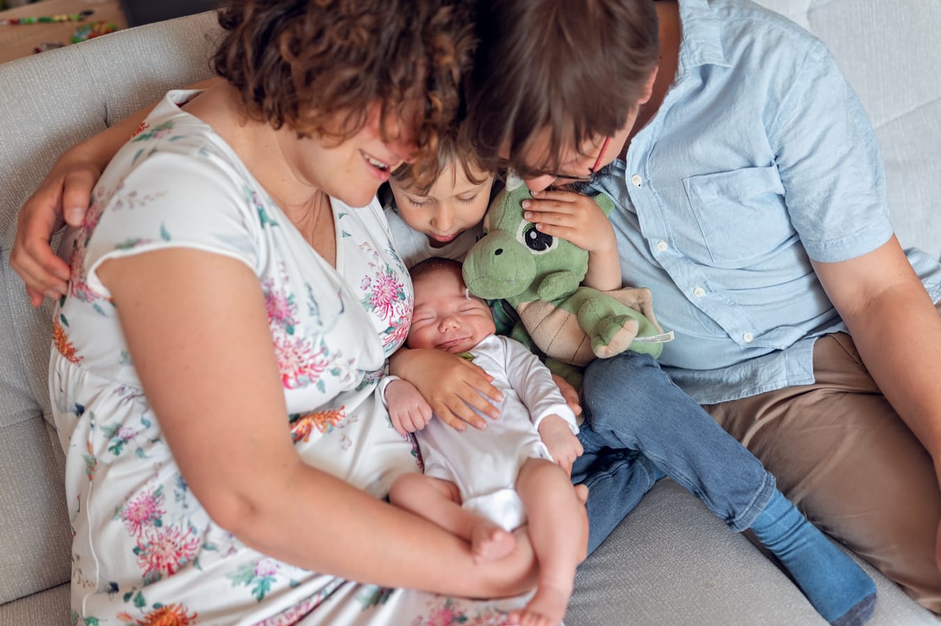 Rodzice na kanapie z synkiem trzymającym zabawkę i noworodkiem — rodzinna sesja noworodkowa Trójmiasto