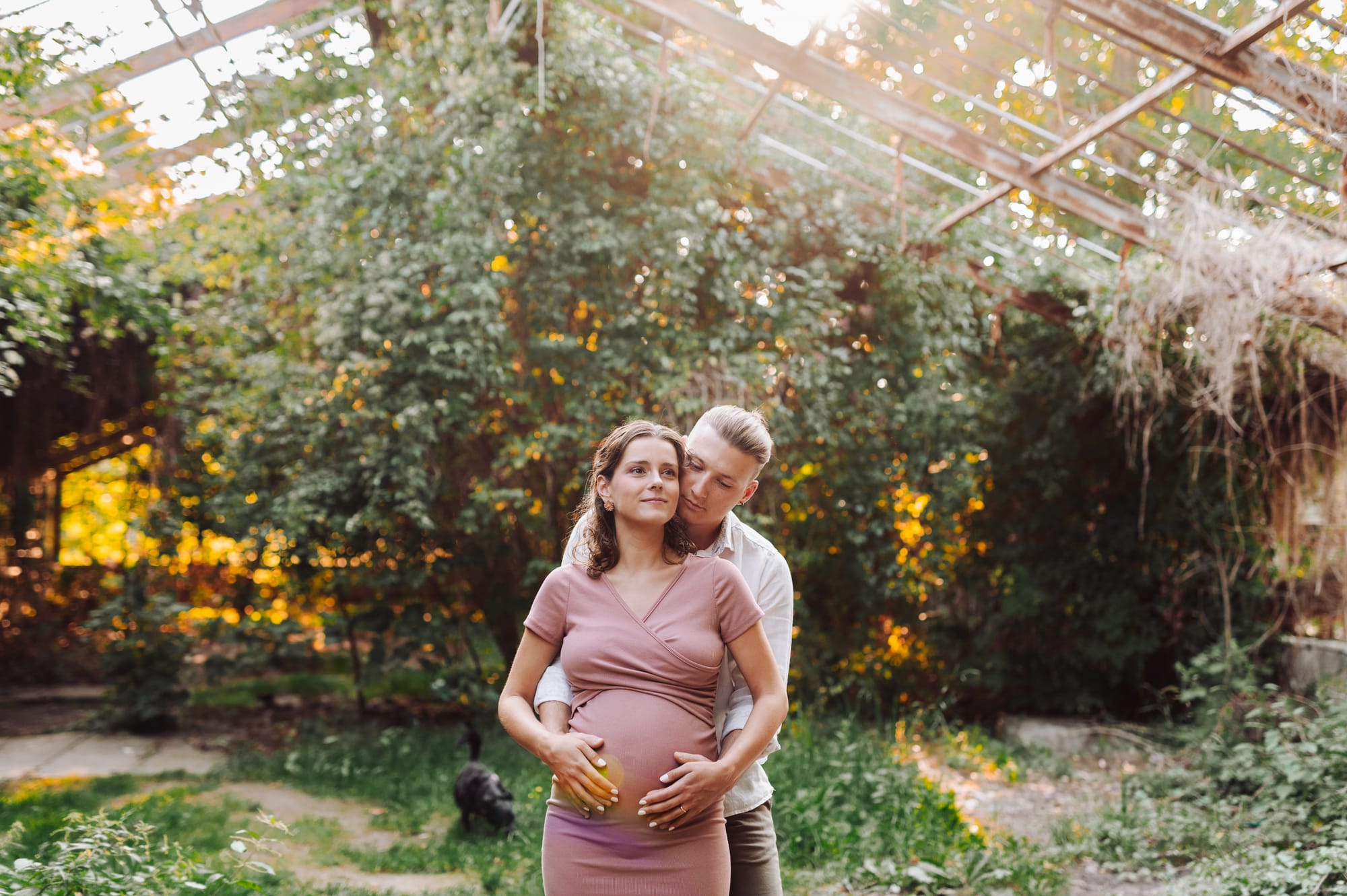 Przyszli rodzice przytulają się w starej opuszczonej szklarni podczas sesji ciążowej w Parku Kolibki w Gdyni