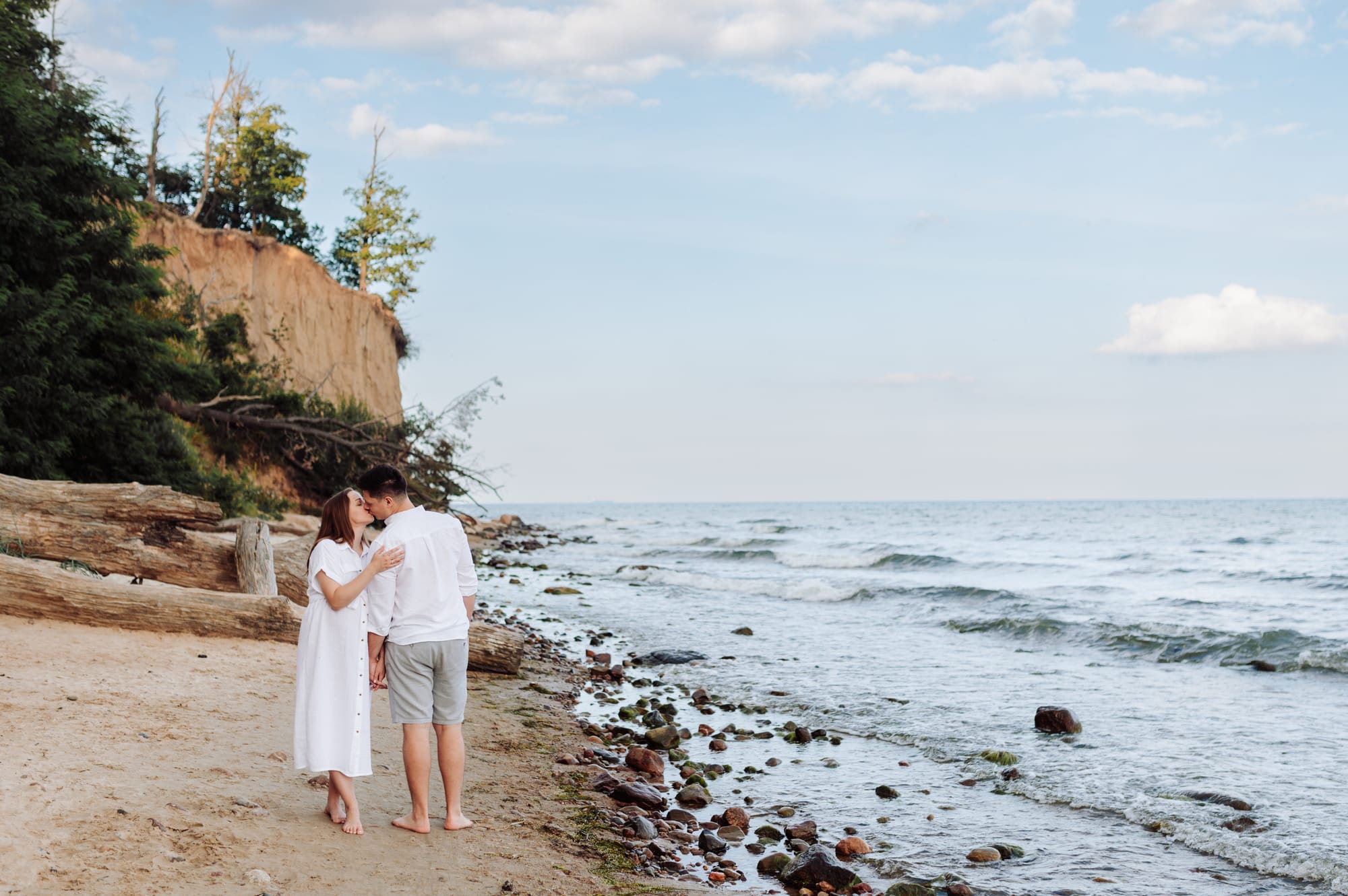Para przytulająca się na brzegu morza z klifem orłowskim w tle — sesja ciążowa w Gdyni