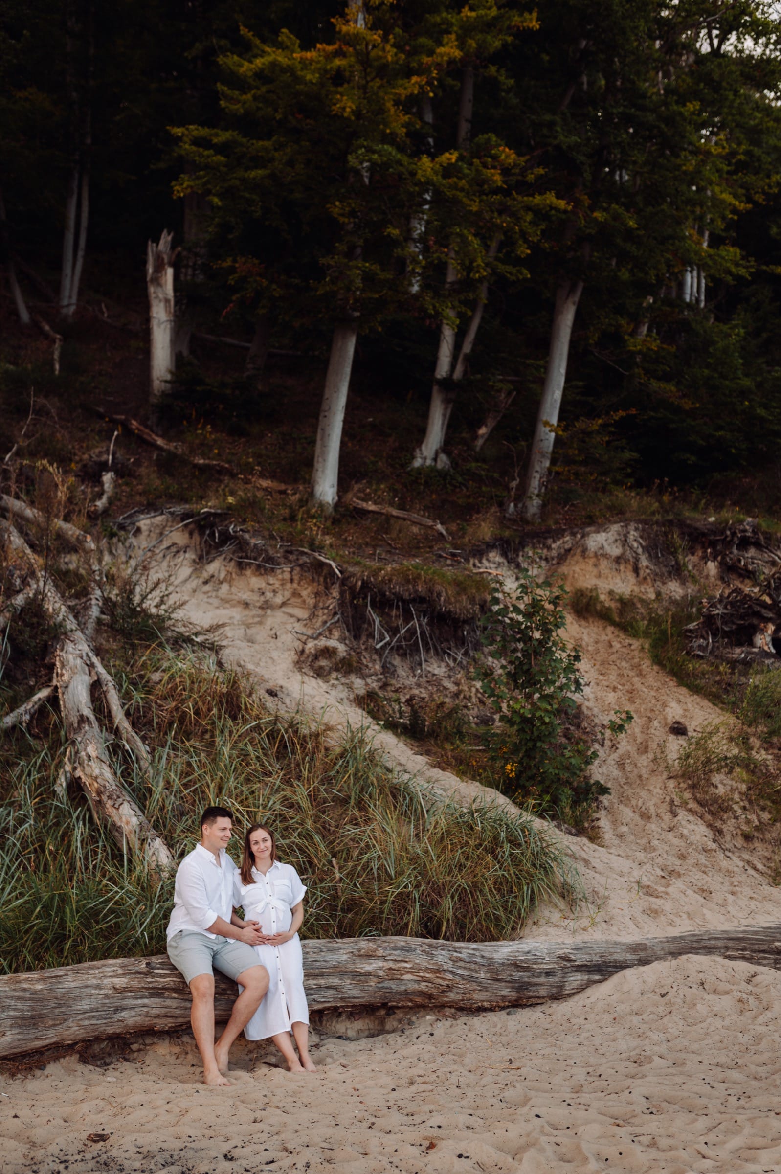 Para siedząca na konarze na plaży w Orłowie, w tle urwisko klifu — sesja ciążowa Trójmiasto