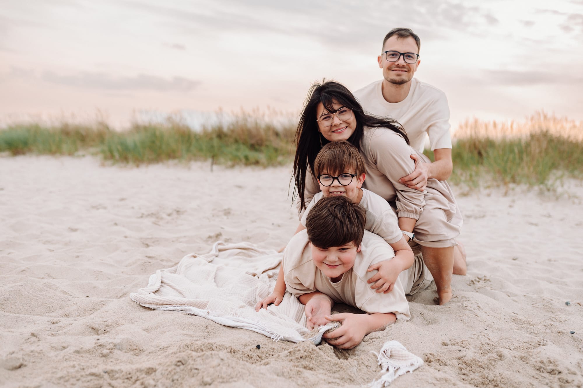 Rodzina z większymi dziećmi w pozycji na kanapkę — radośni i uśmiechnięci podczas sesji nad morzem w Rewie