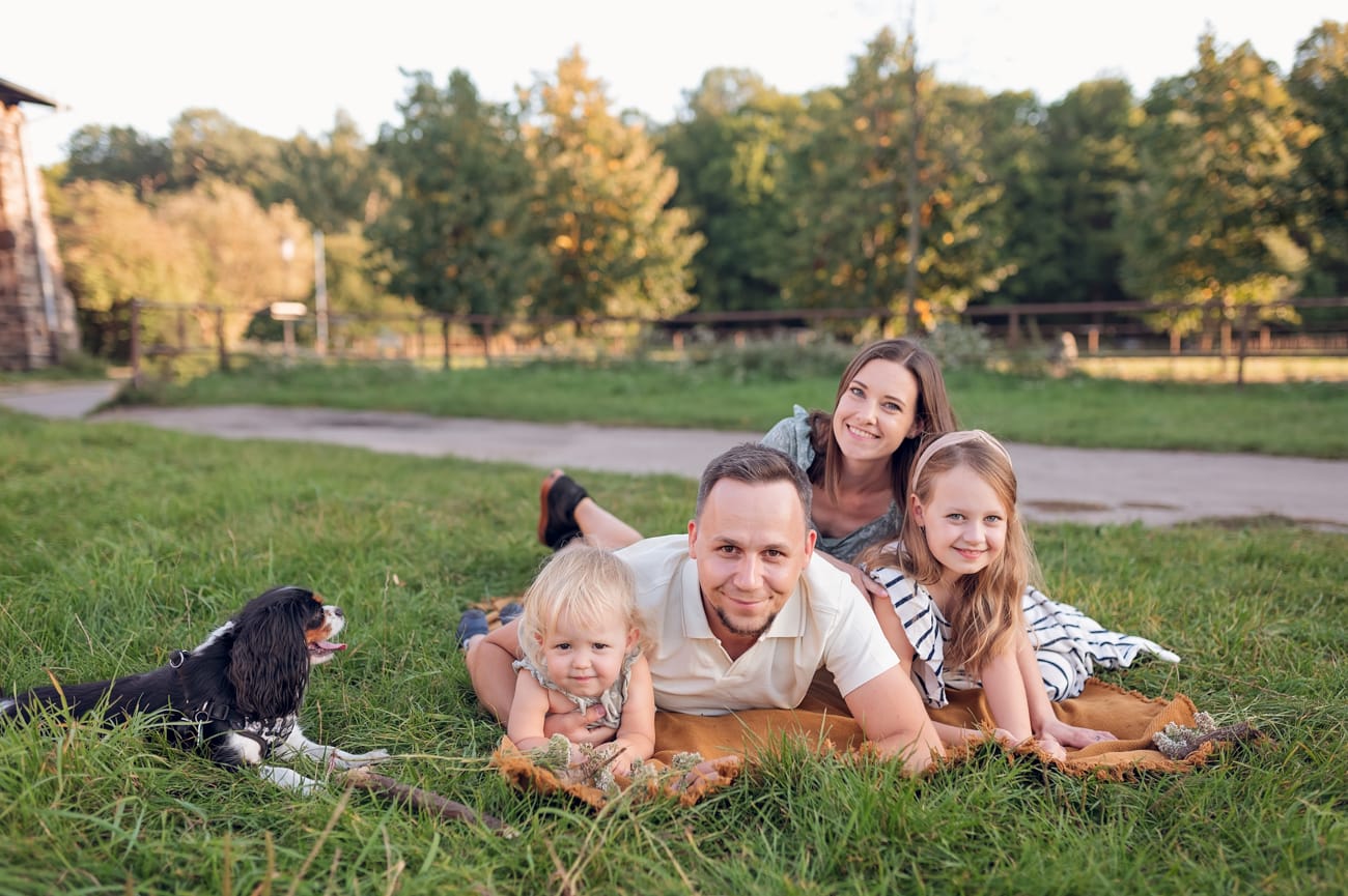 Rodzina z psem leżąca na kocu na łące przy zabytkowych stajniach — sesja rodzinna Kolibki Gdynia