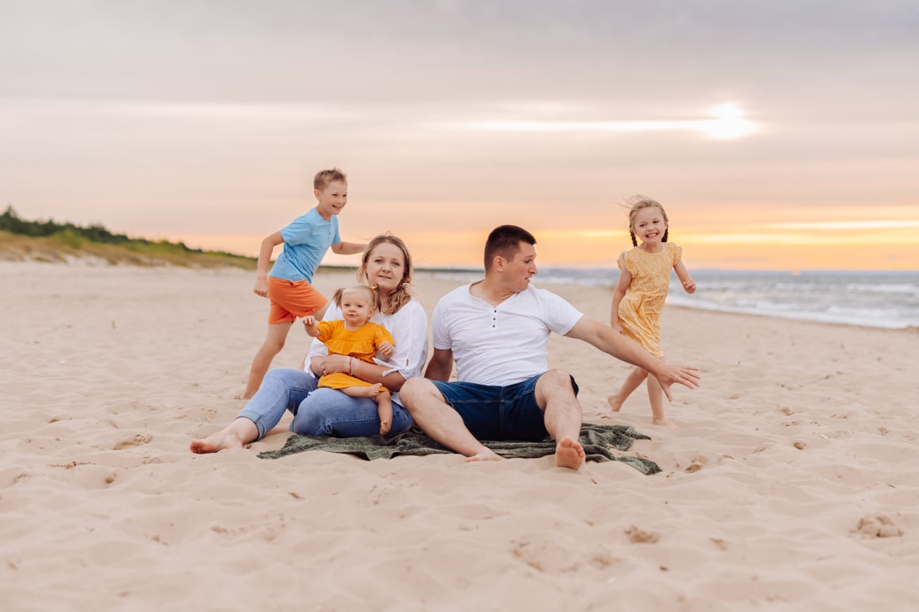 Rodzina bawiąca się na plaży na Wyspie Sobieszewskiej — za nimi dramatyczne ciemne chmury przebite złoto-pomarańczowym zachodzącym słońcem
