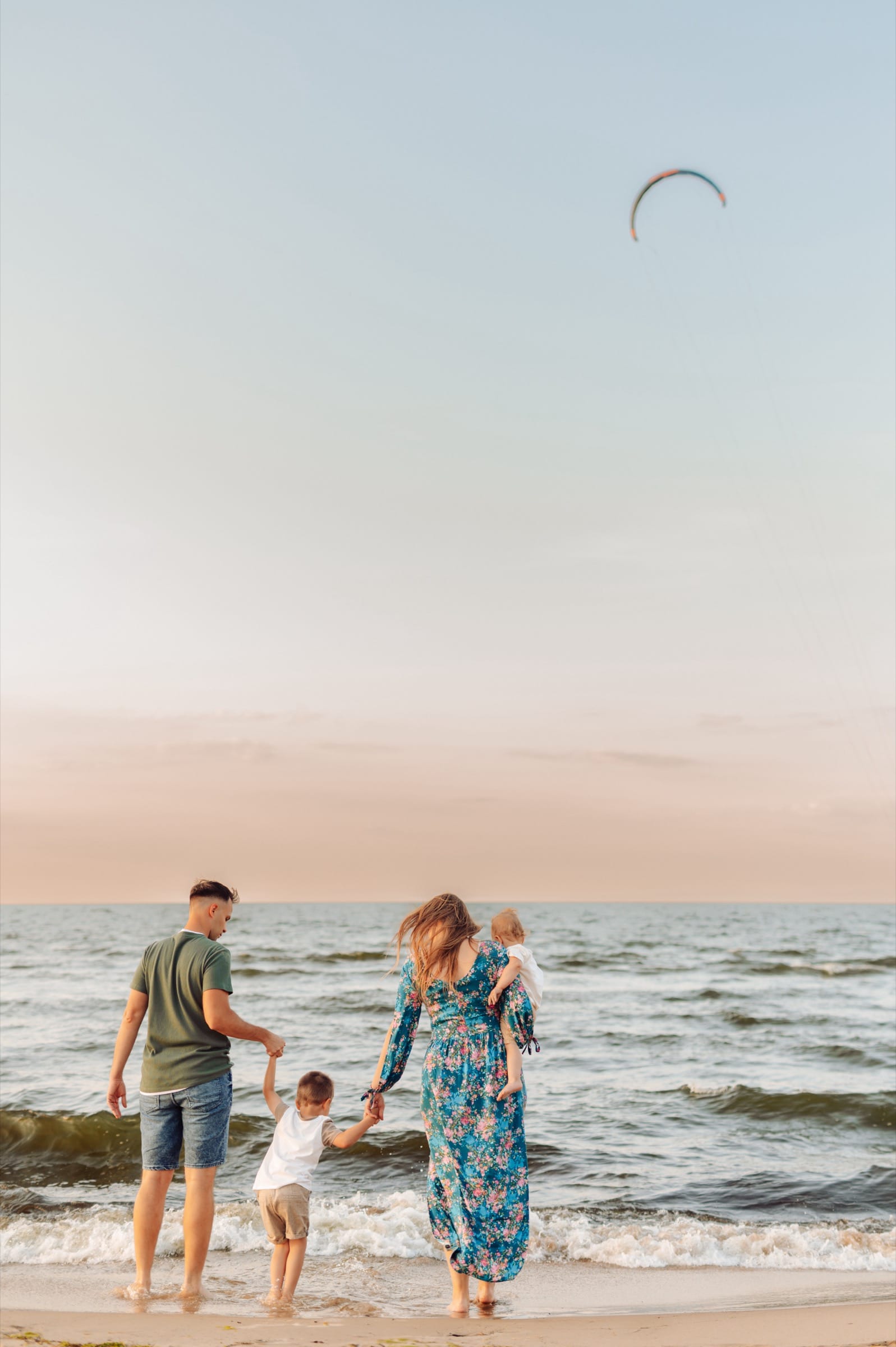 Rodzina na tle morza o zachodzie słońca, na niebie widać paralotnie — sesja rodzinna Sobieszewo