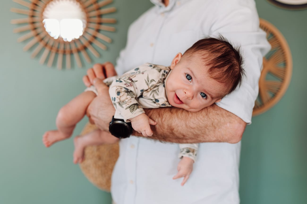 Tata trzyma uśmiechniętego niemowlaka na rękach — lifestyle sesja niemowlęca Trójmiasto