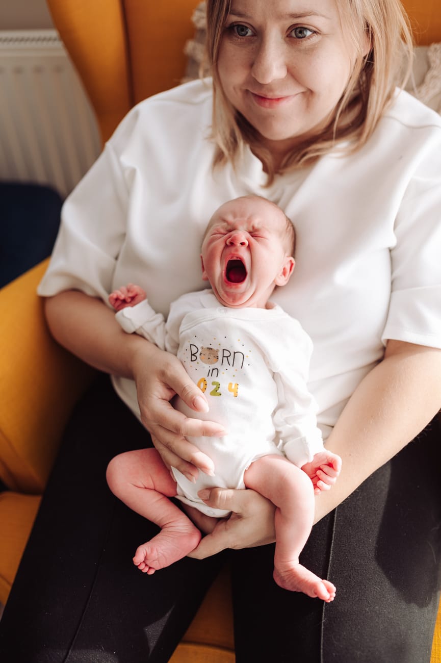 Ziewający noworodek w ramionach mamy sesja w domu Gdynia