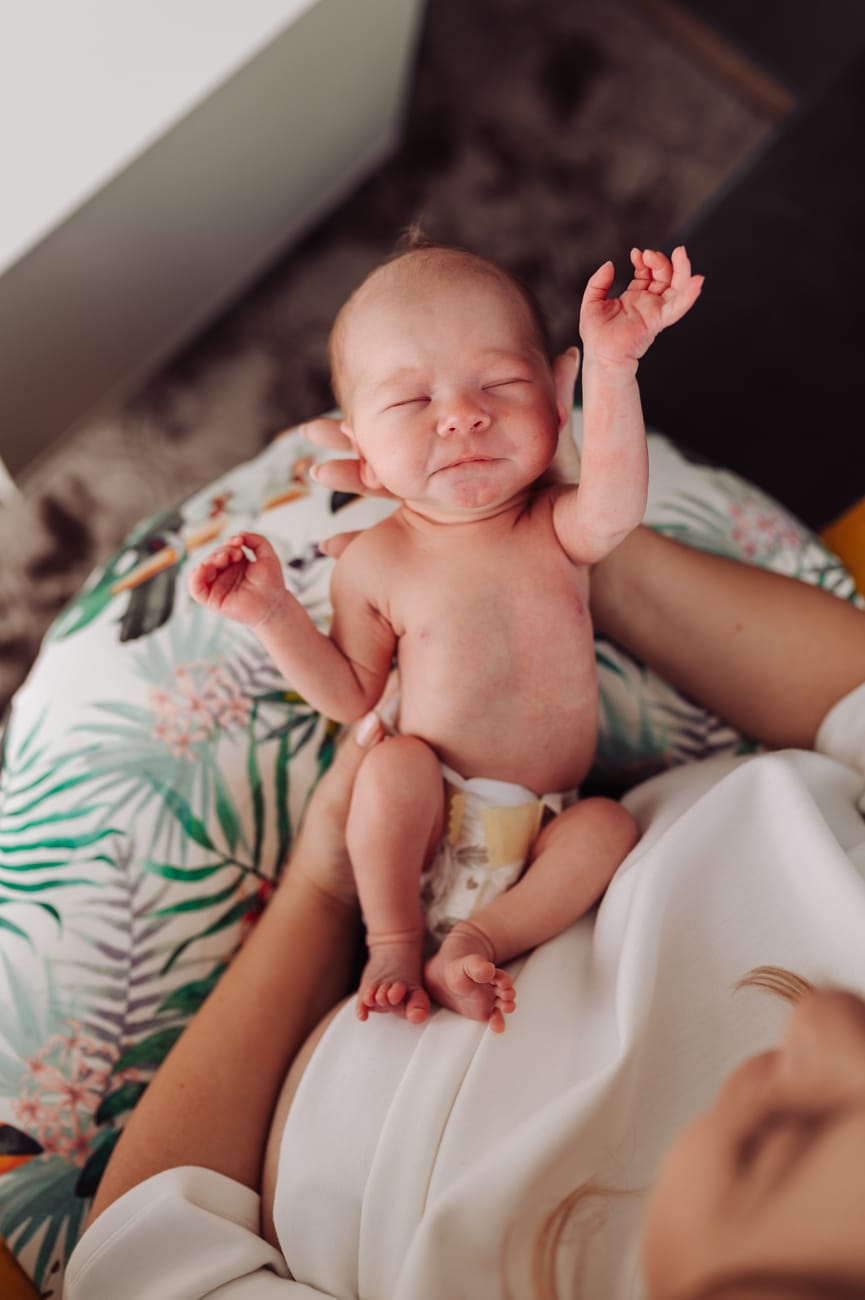 Noworodek, który przeciągajacy się na rękach mamy zaraz po karmieniu piersią. 