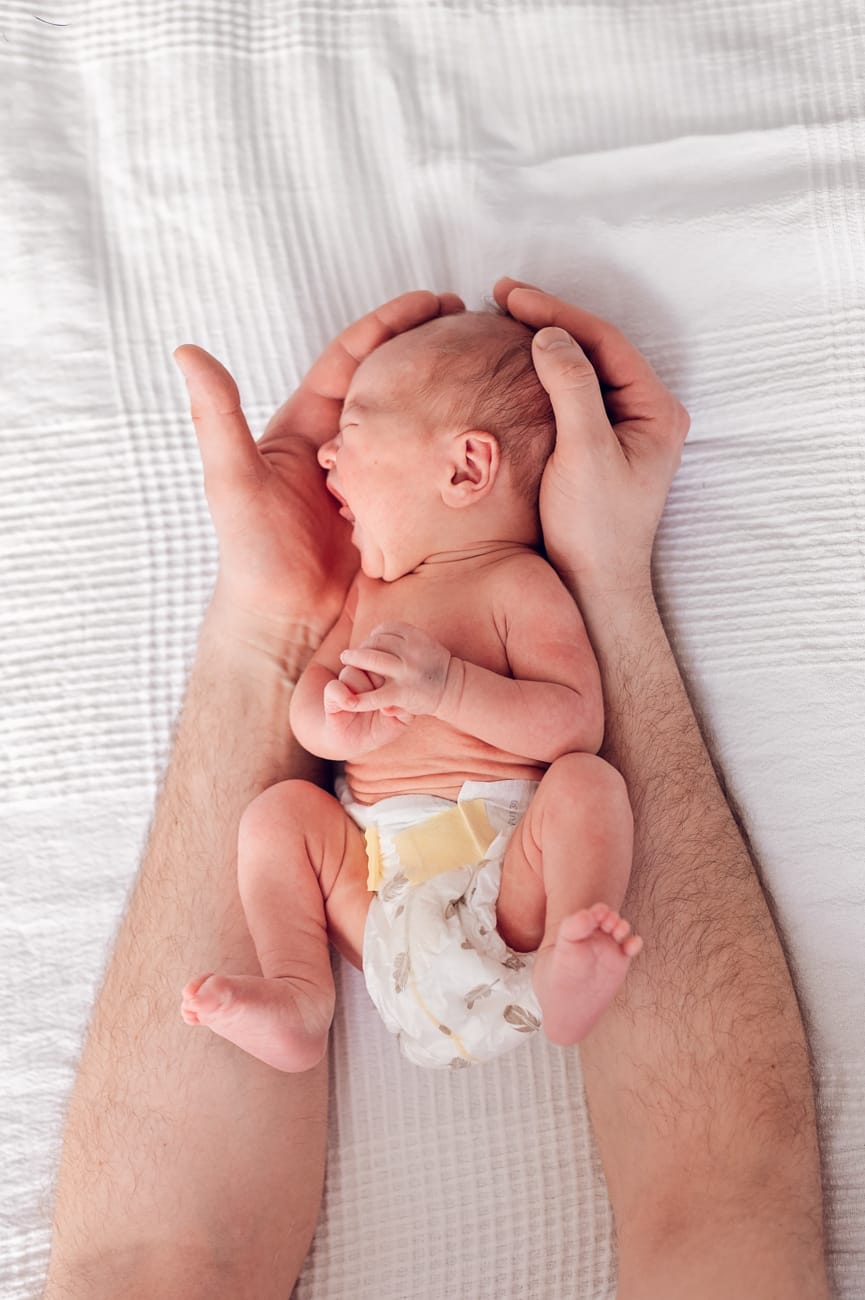 Płaczący noworodek między dłońmi taty sesja noworodkowa lifestyle Gdynia
