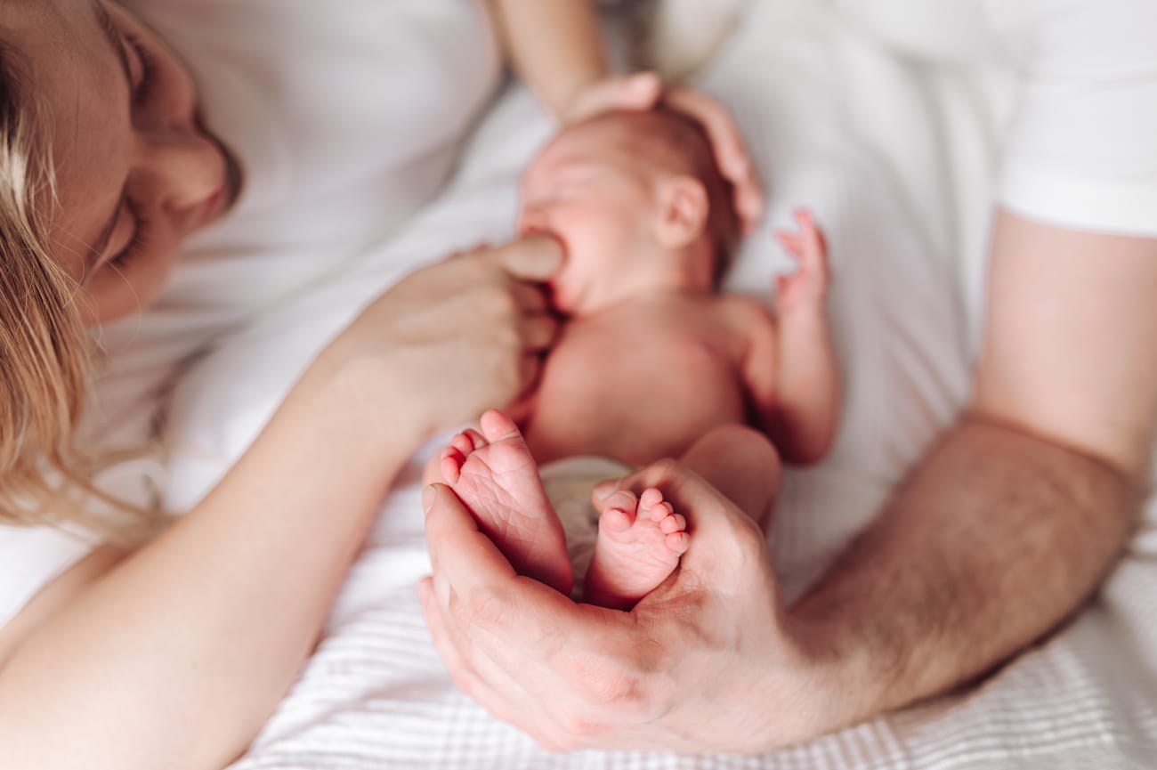 Zbliżenie stópek noworodka, który w tle ssie palec mamy.
