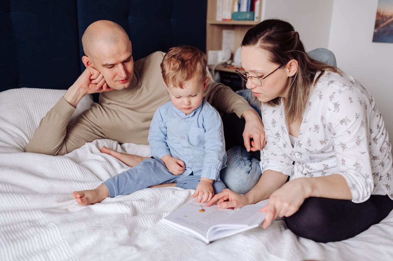 Chłopiec z rodzicami czytają książeczkę sesja rodzinna w domu
