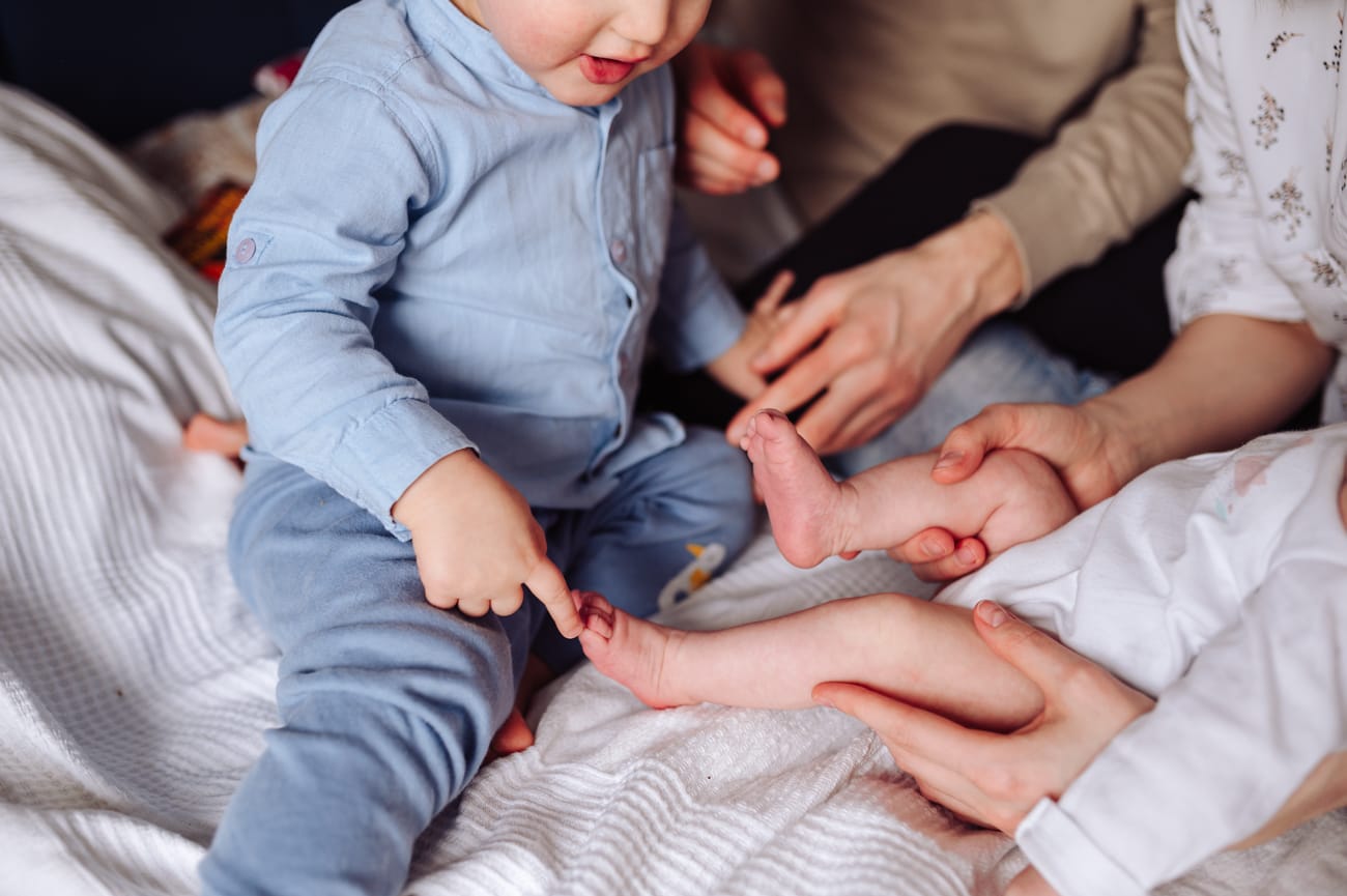 Brat dotyka stópki noworodka sesja rodzinna w domu