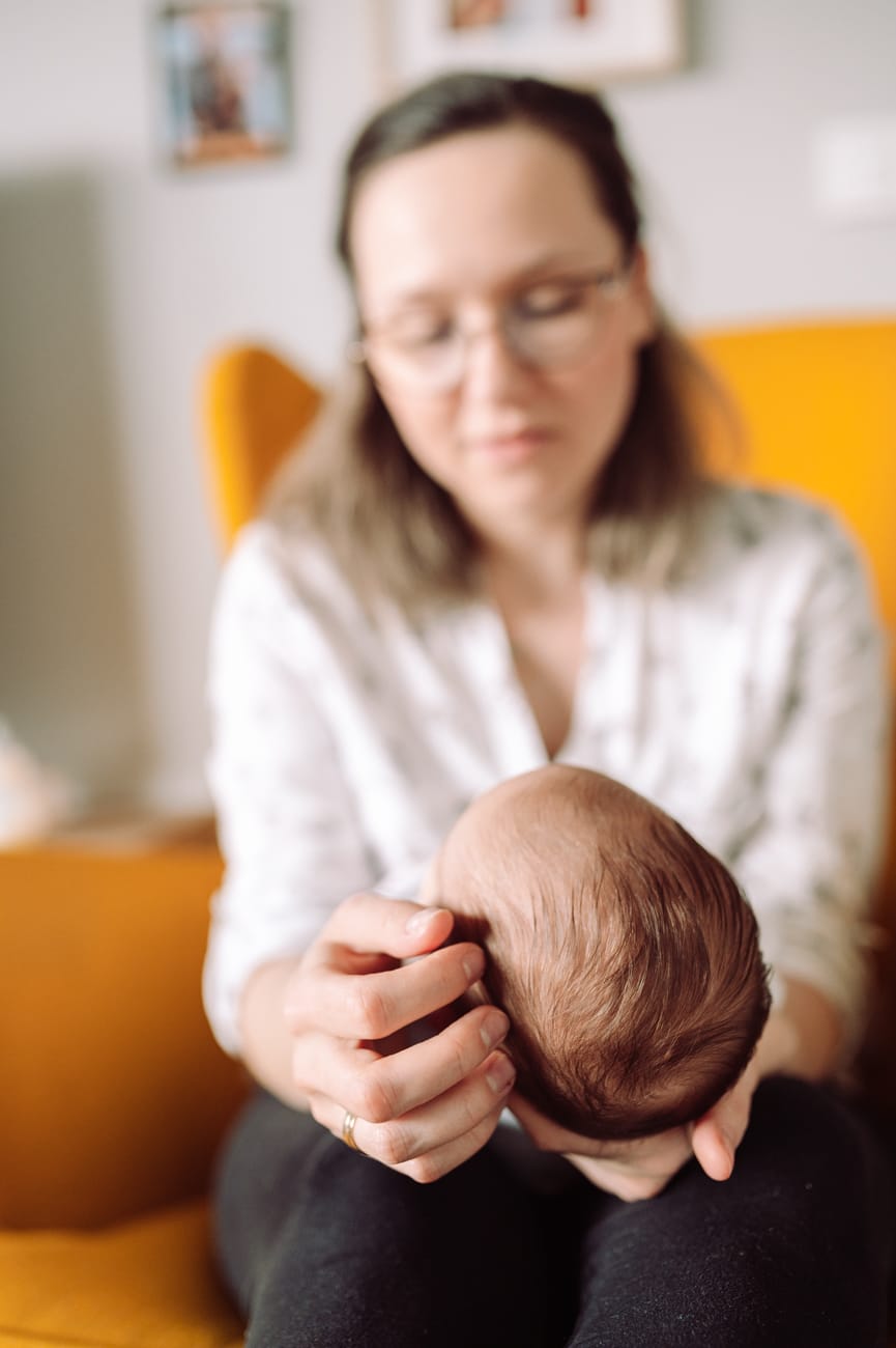 Główka noworodka w dłoniach mamy sesja w domu