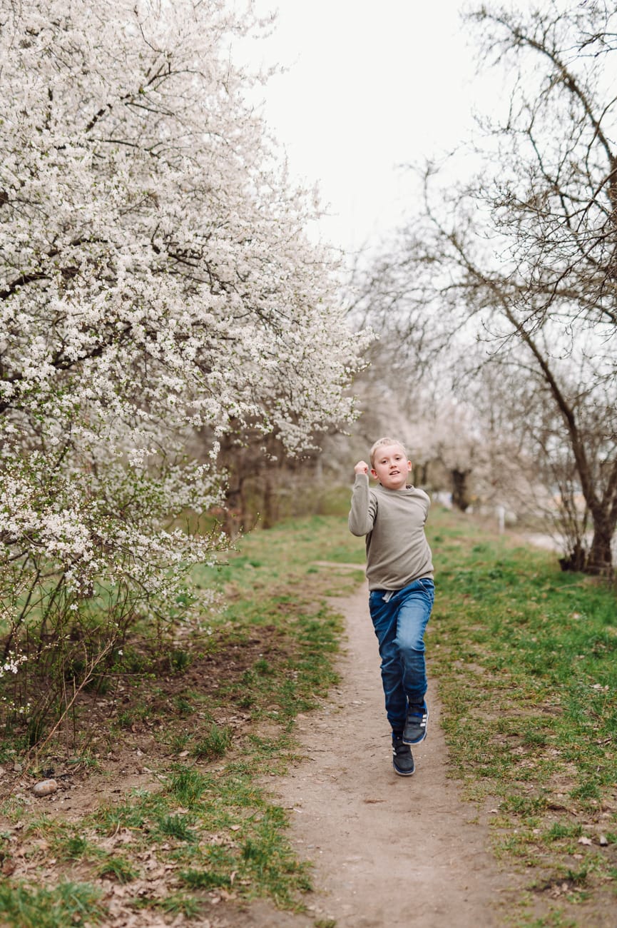 Chłopiec biegnie alejką w kwiatach sesja dziecięca