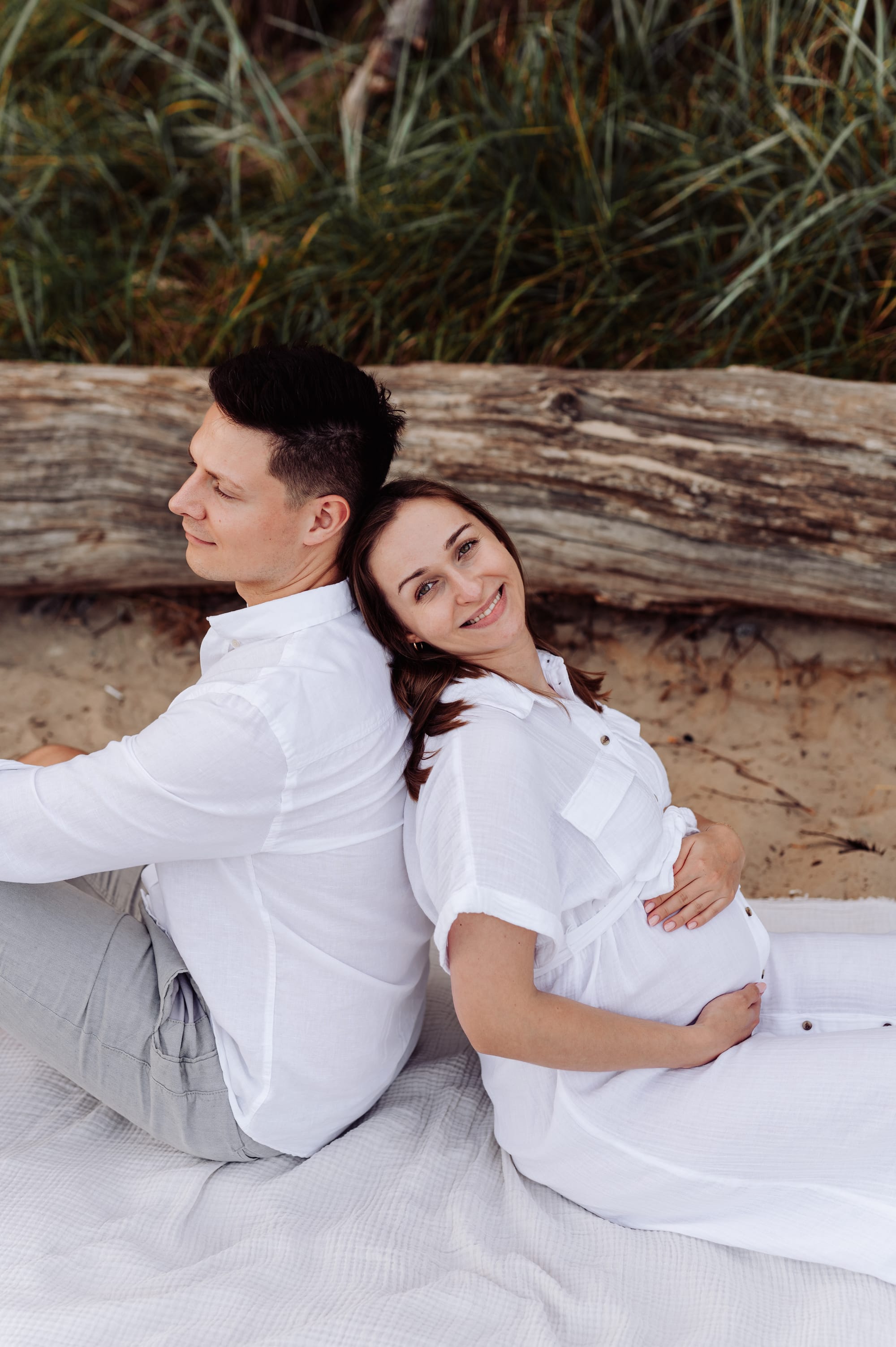 Przyszła mama siedzi na plaży plecami do partnera i wpatruje się w morze — sesja ciążowa Orłowo Gdynia, fotograf Natalia Kobylak