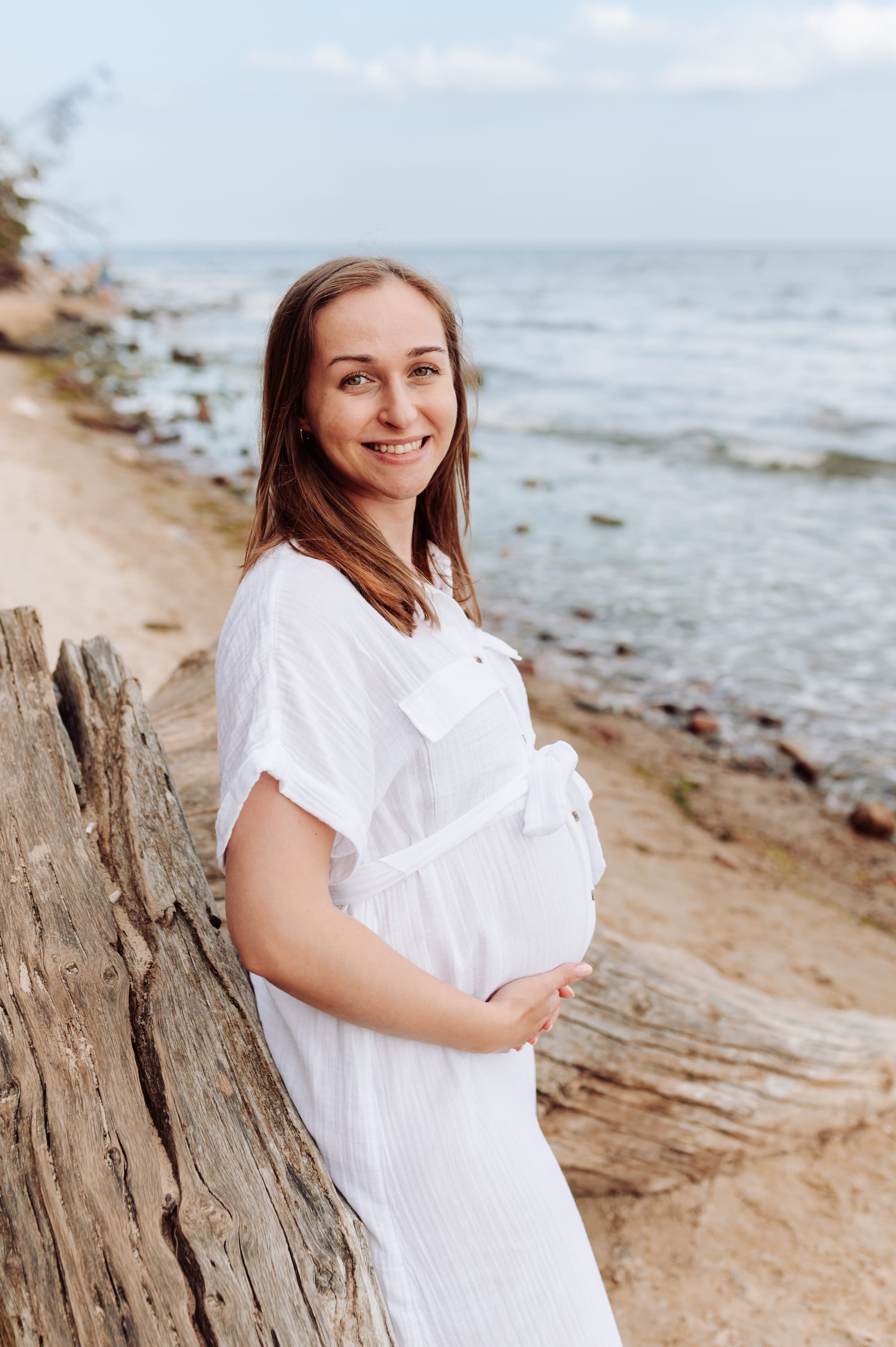Mama w ciąży opiera się o drzewo na plaży w Orłowie i uśmiecha do obiektywu — sesja ciążowa Gdynia, fotograf Natalia Kobylak