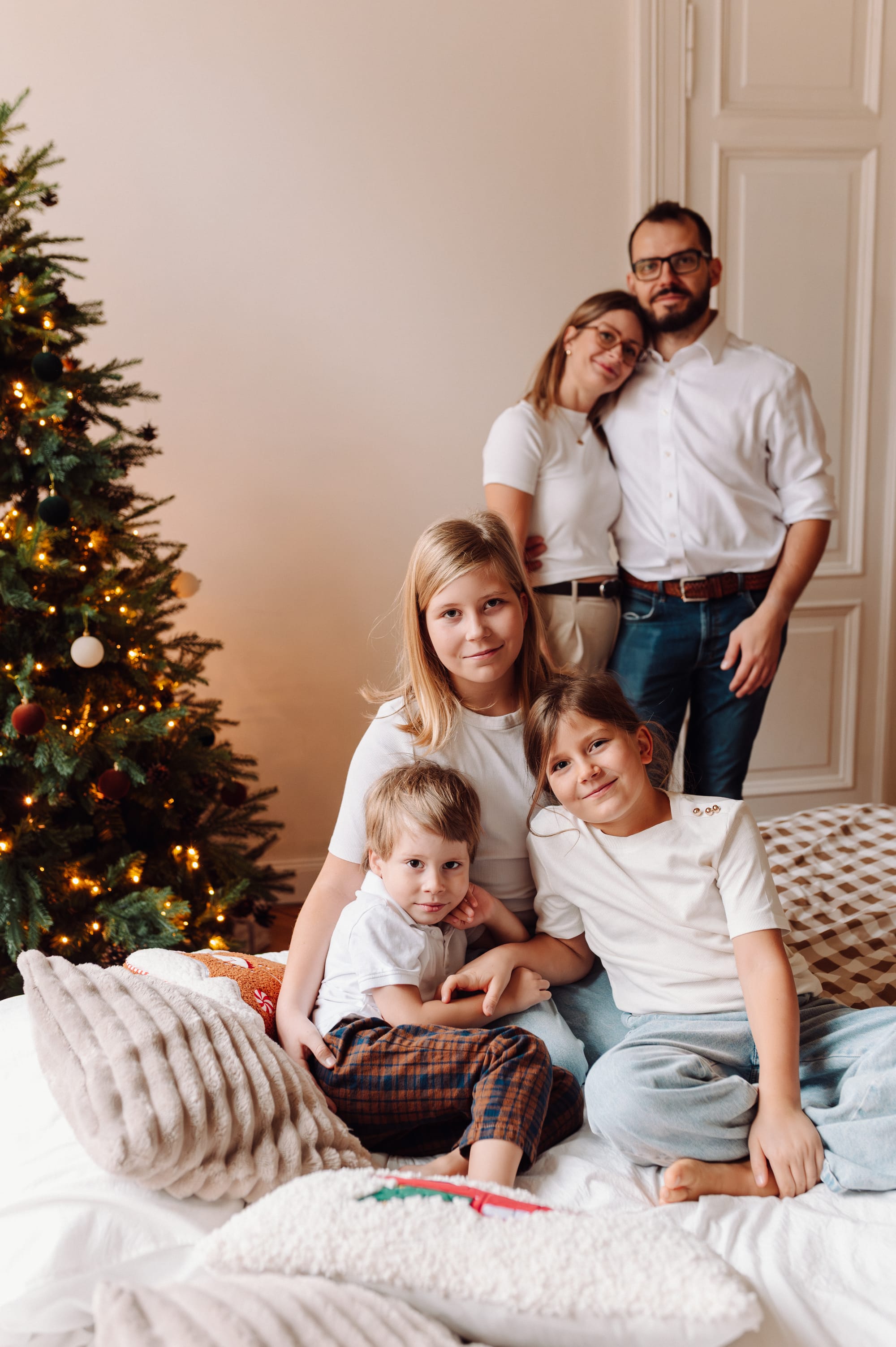 Dzieci siedzące na łóżku, w tle przytuleni rodzice, sesja świąteczna Studio Matejki