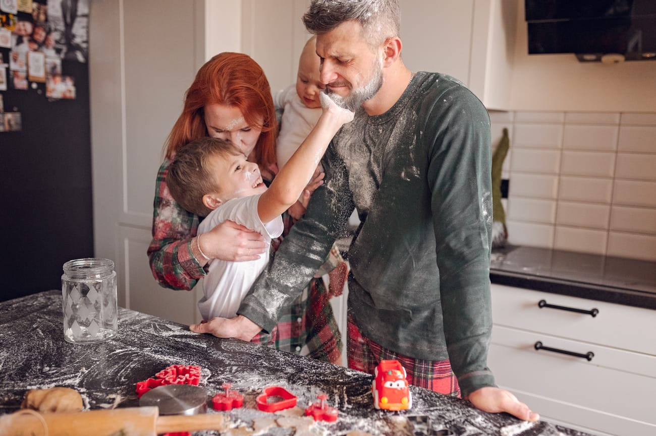 Rodzina w piżamach piecząca pierniczki w kuchni, syn smaruje tatę mąką, domowa sesja świąteczna, Trójmiasto — fotograf Natalia Kobylak