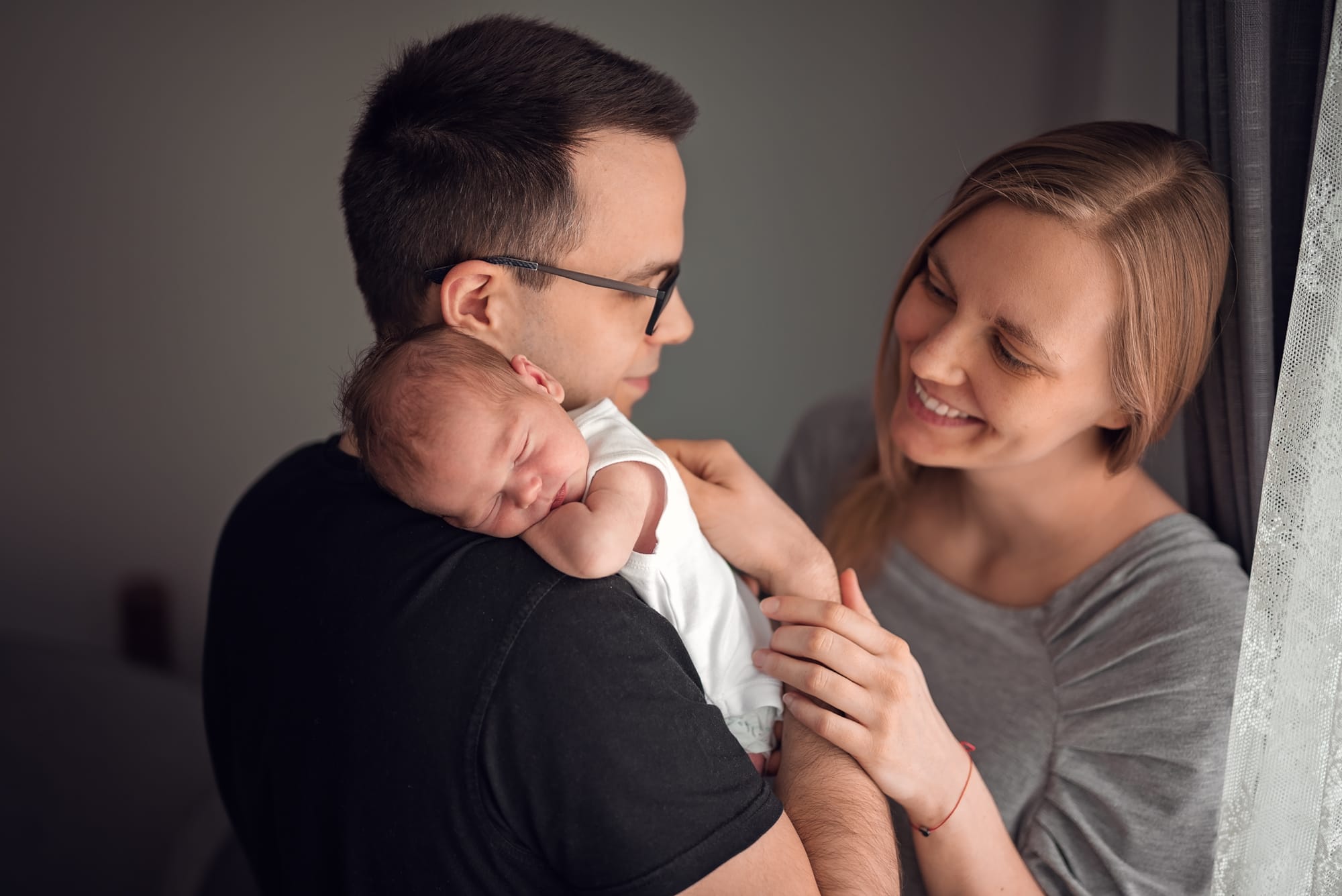 Mama patrzy na noworodka na ramieniu taty sesja w domu
