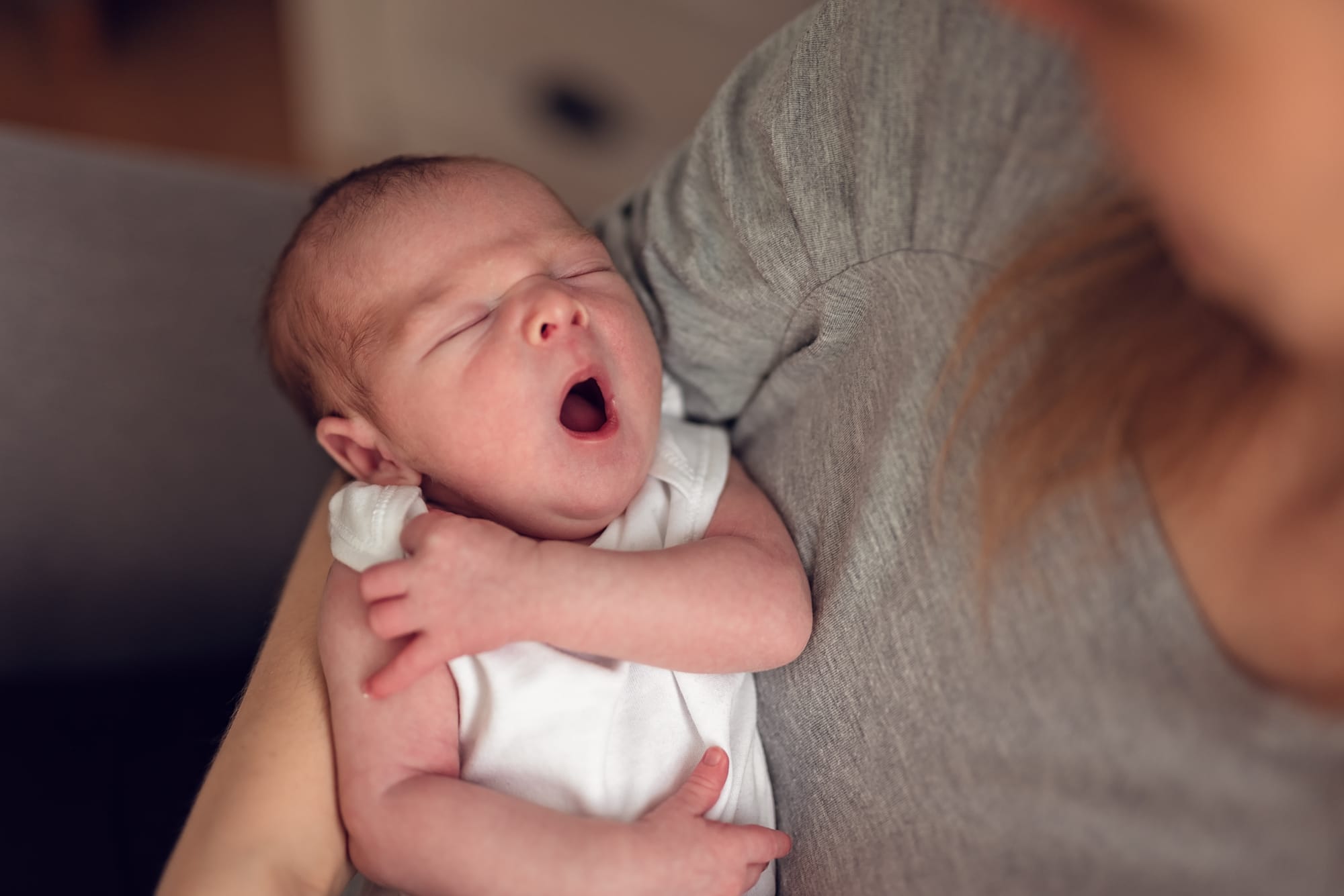 Ziewający noworodek w ramionach mamy sesja w domu