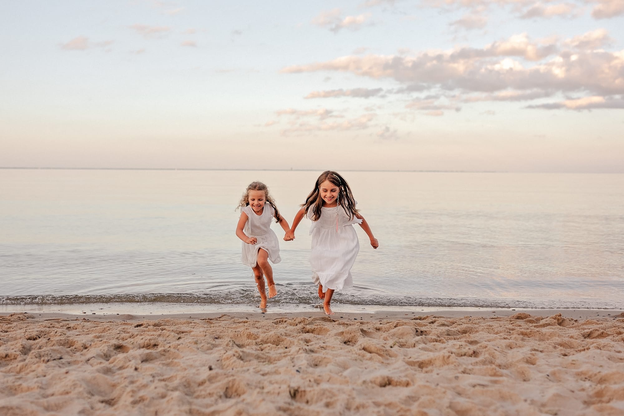 Siostry biegną po plaży dopasowane sukienki sesja rodzinna