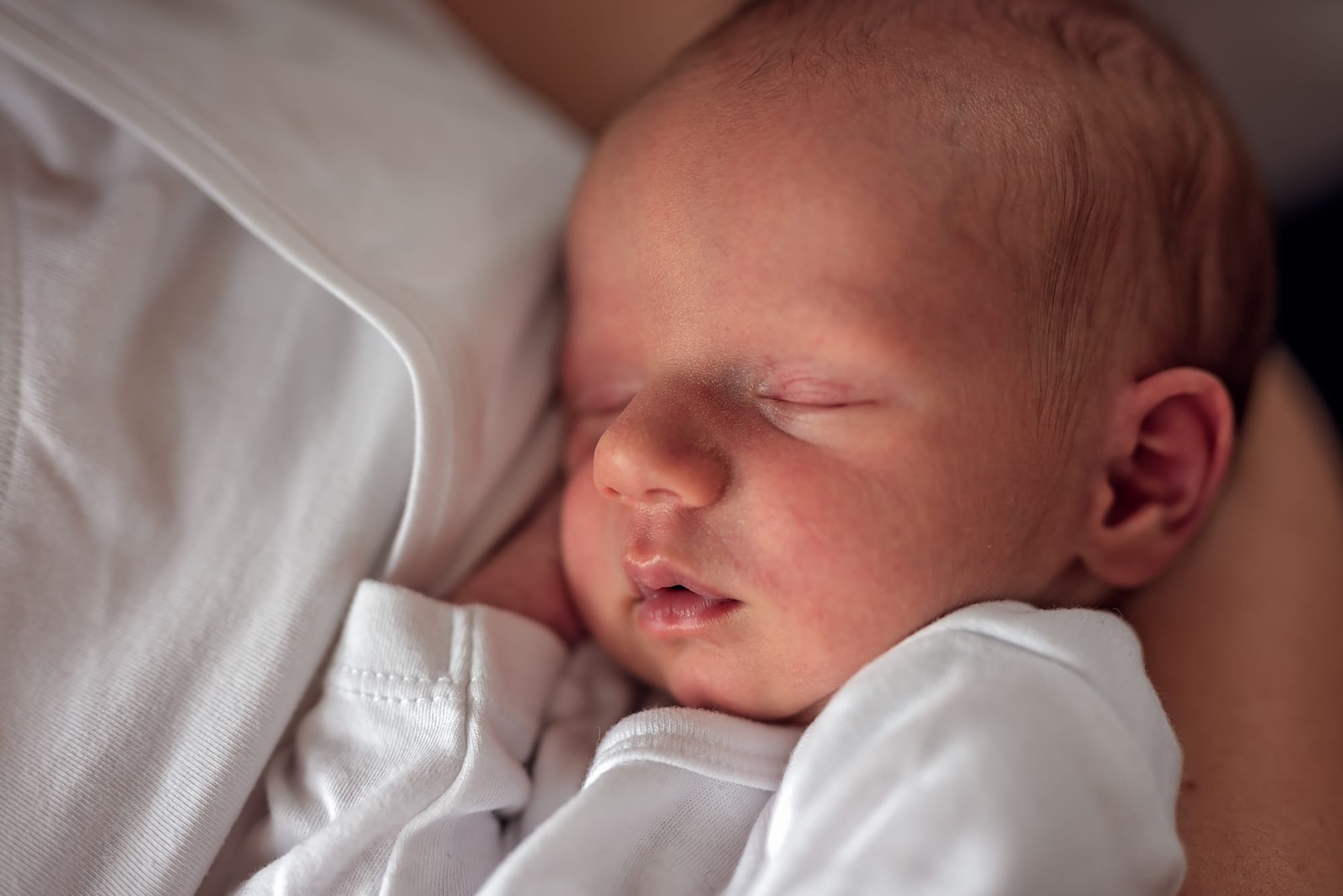 Noworodek śpiący w ramionach w trakcie domowej sesji. 