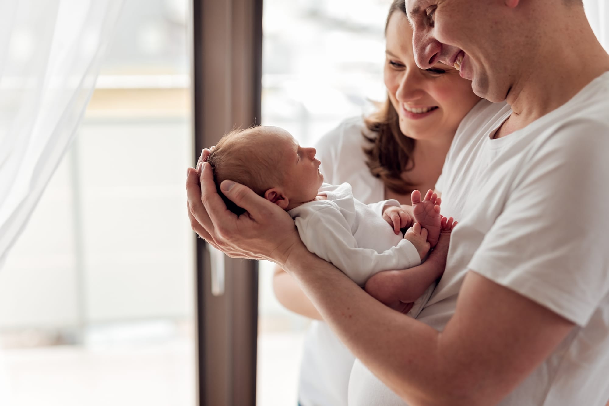 Rodzice w jasnych ubraniach z noworodkiem sesja w domu