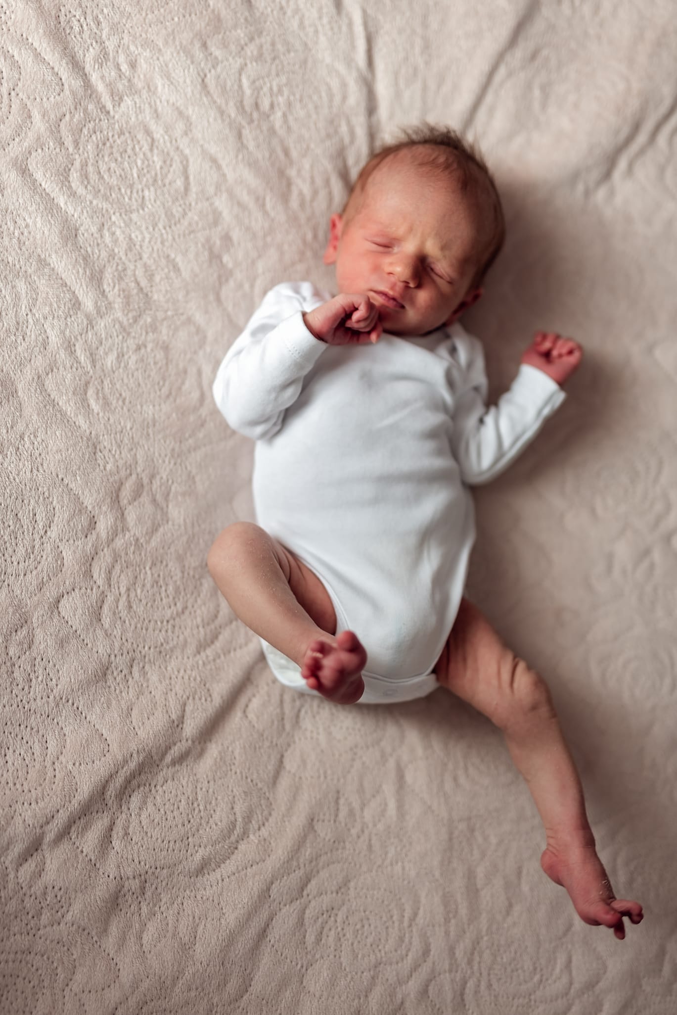 Noworodek przeciąga się na łóżku sesja noworodkowa