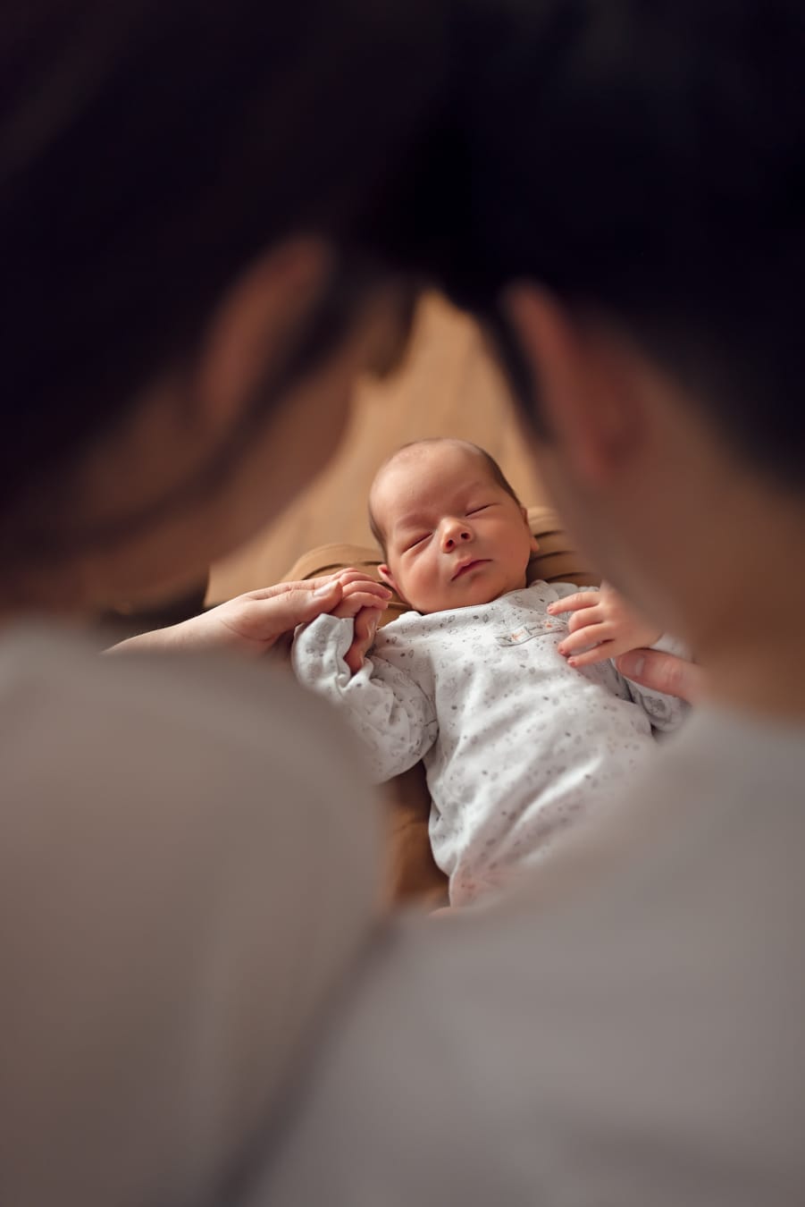 Widok na noworodka spomiędzy rodziców, którzy spoglądają na niego. 