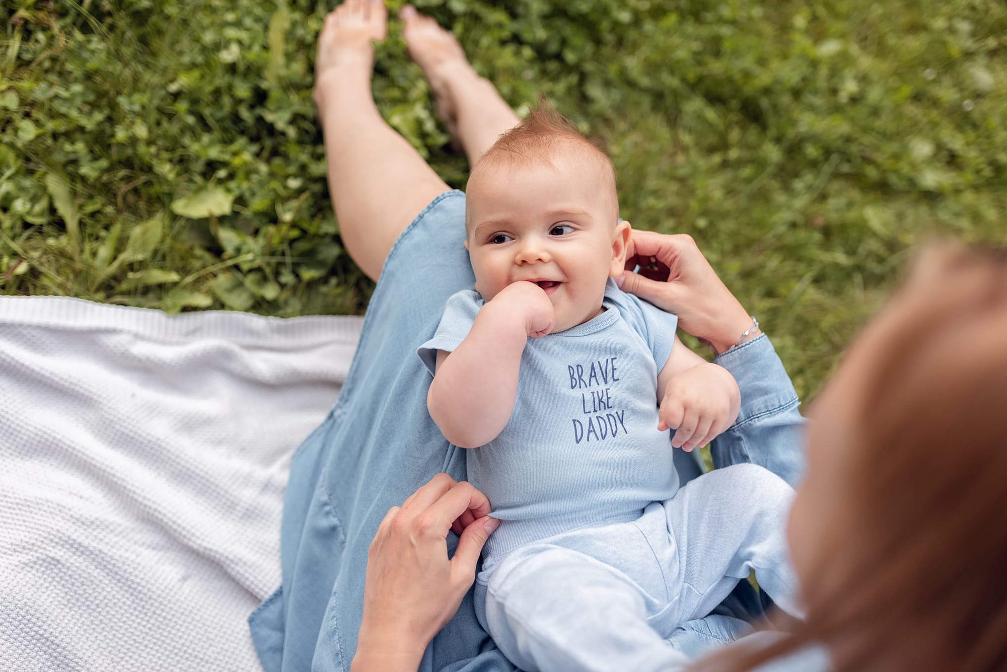 Niemowlak leży na kolanach u mamy sesja z niemowlakiem w plenerze
