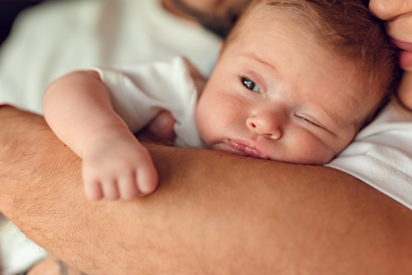 Przysypiające niemowlę tulące się do ramienia taty.