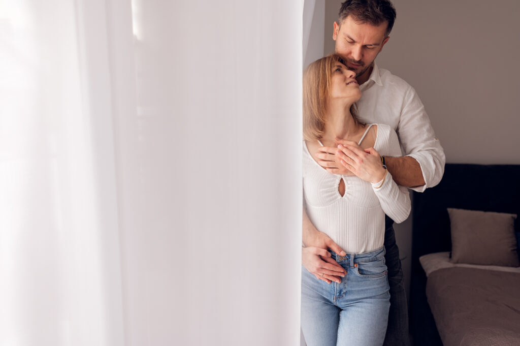 Para przytulająca się przy oknie w domu — sesja dla par Gdańsk