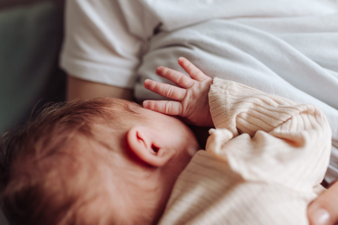 Dłoń noworodka przy piersi mamy sesja noworodkowa