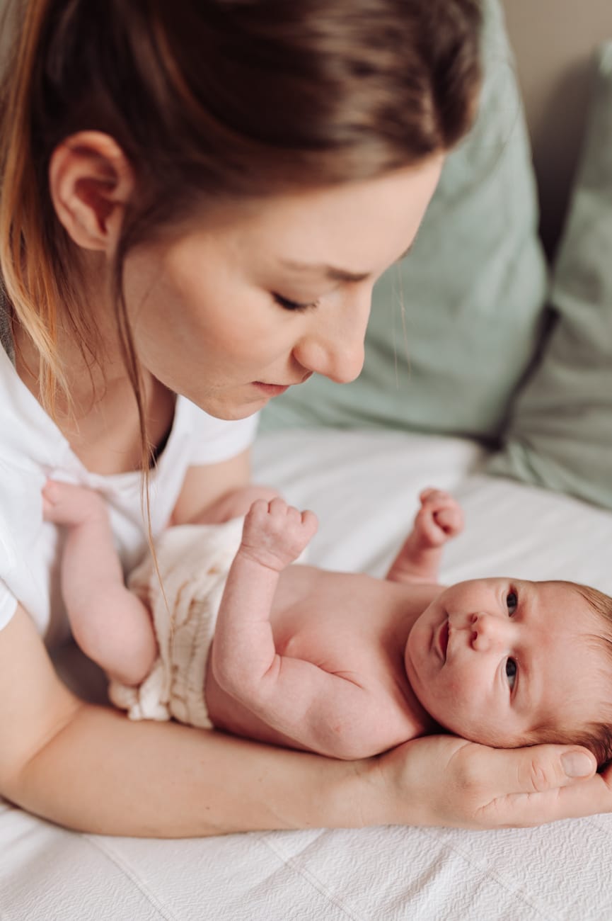 Mama przytula noworodka naturalne światło sesja w domu
