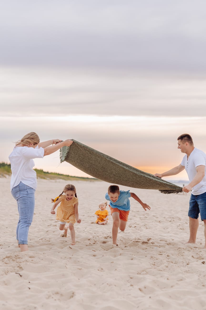 Dzieci biegną pod kocem sesja rodzinna na plaży