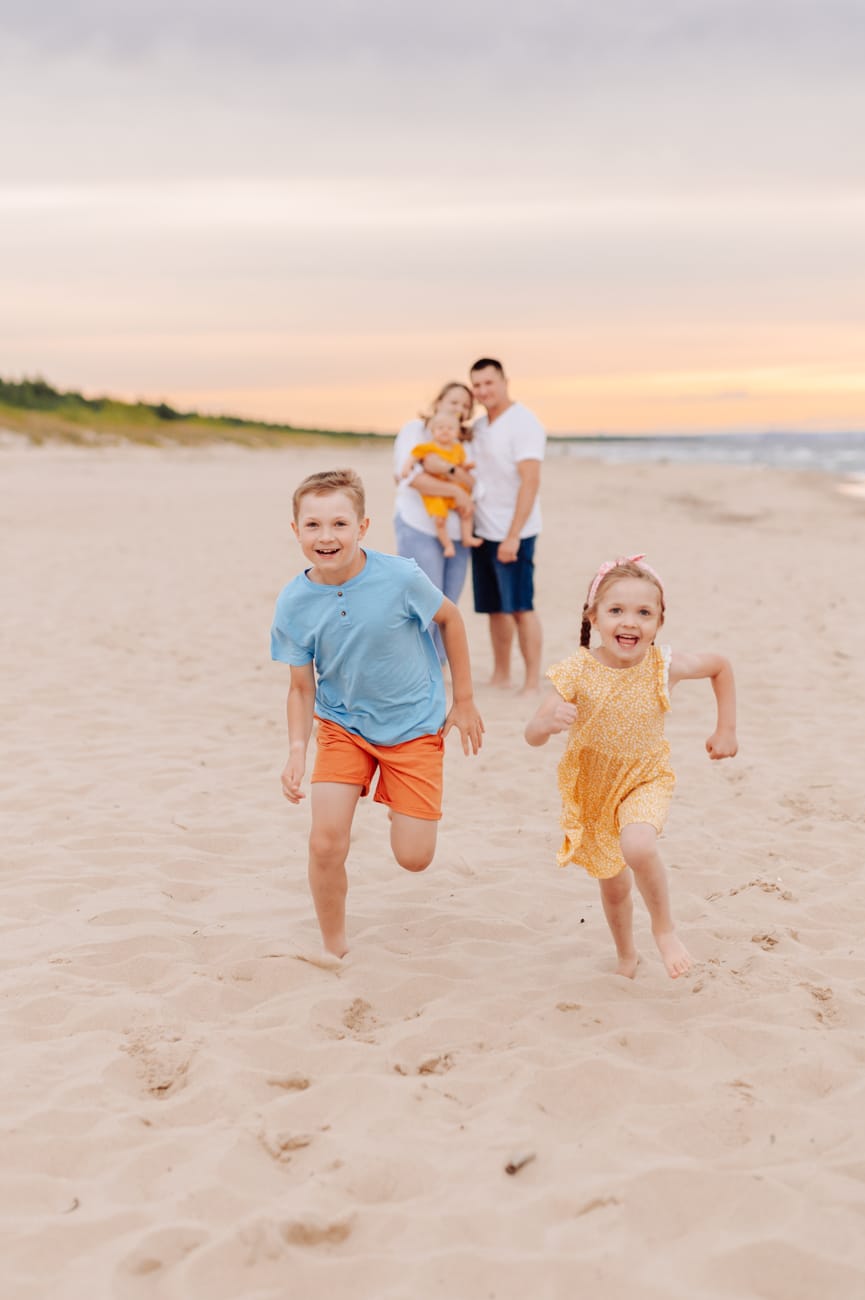 Dzieci biegną po plaży rodzice z niemowlakiem w tyle