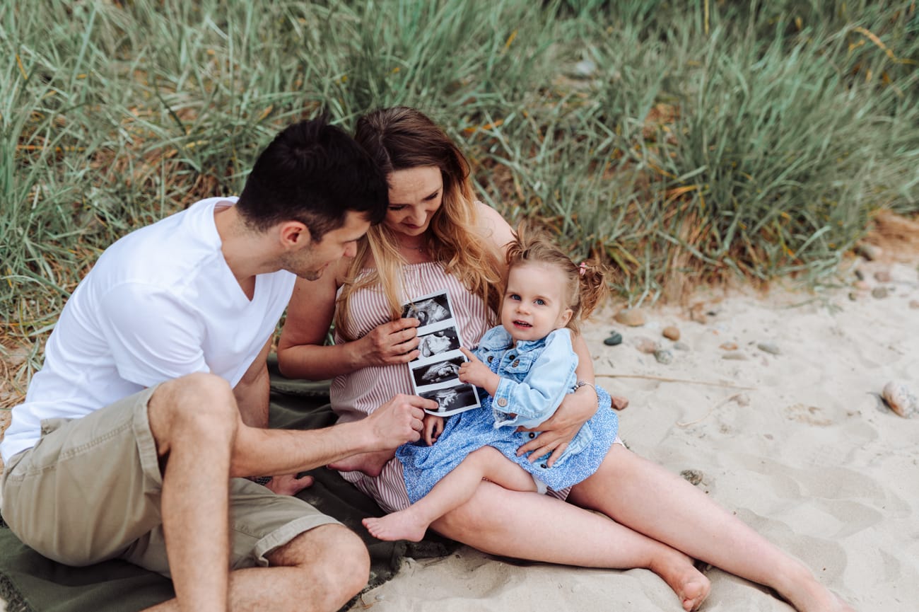 Rodzina ogląda zdjęcie USG na plaży sesja ciążowa