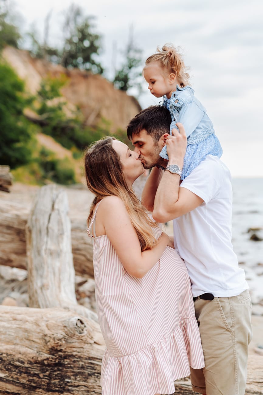 Para całuje się córka na ramionach taty sesja ciążowa