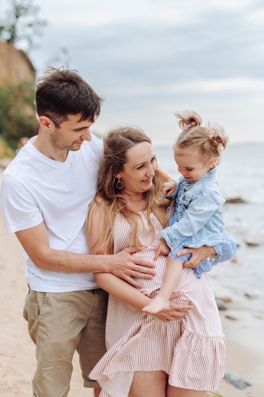 Rodzice tulą córkę na tle morza sesja ciążowa