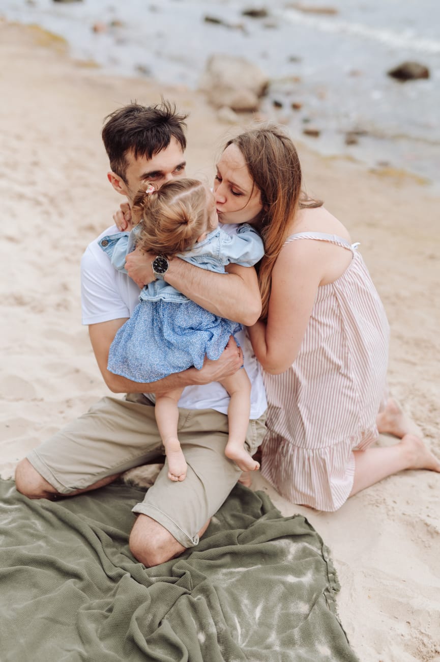 Rodzice całują córkę na plaży sesja ciążowa Gdynia
