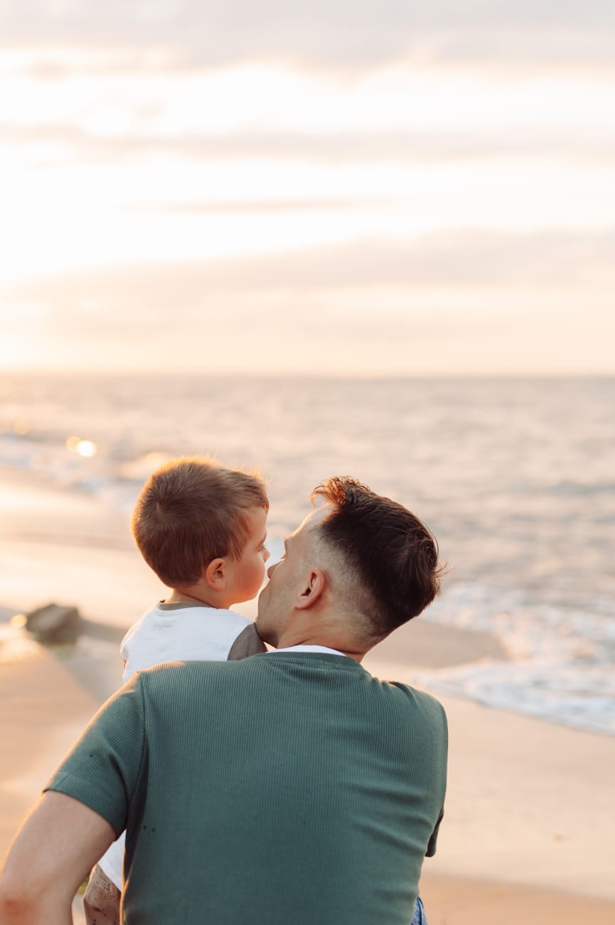Tata i syn patrzący na morze o zachodzie słońca.