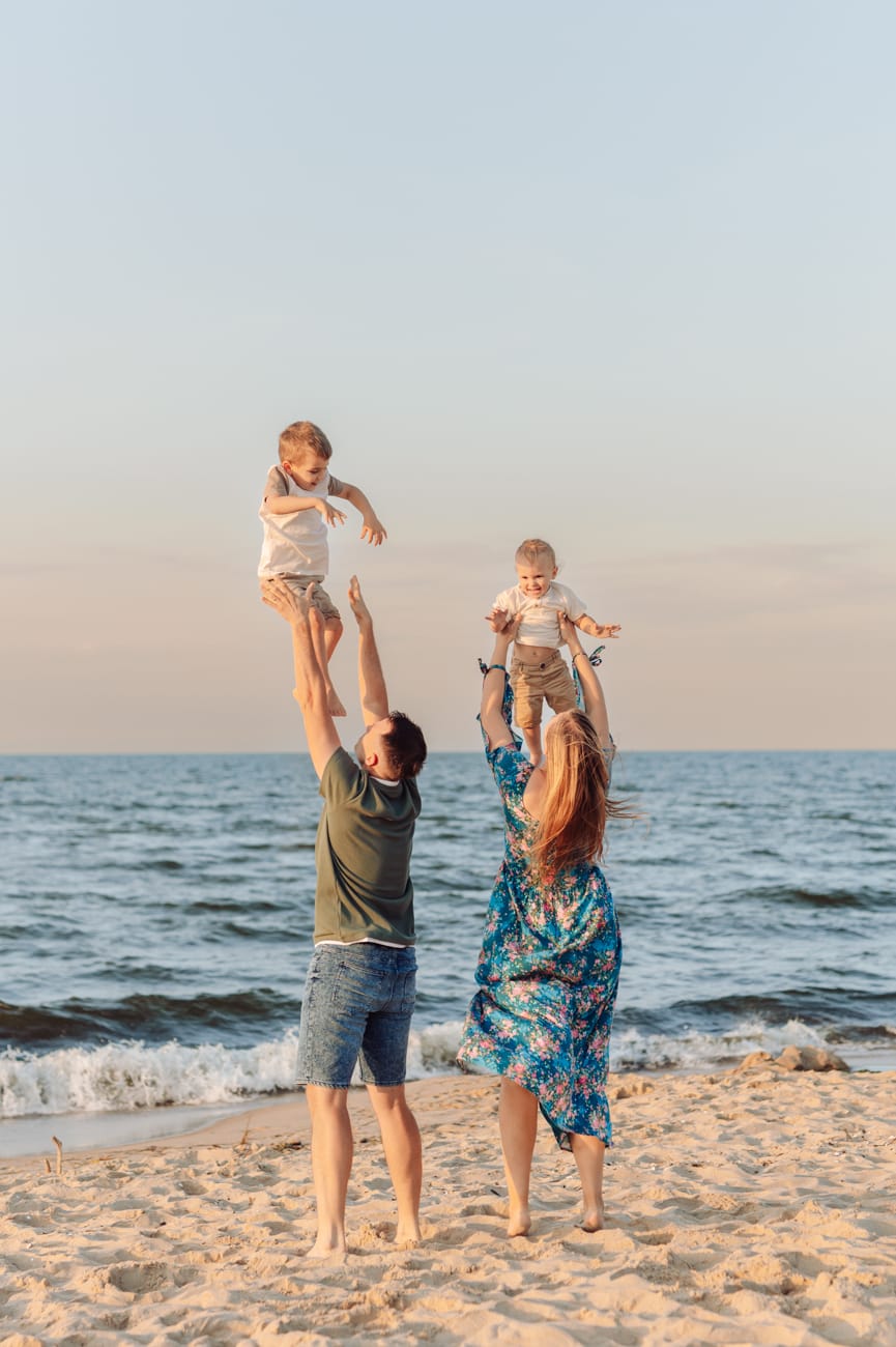 Rodzice podrzucają dzieci brzeg morza zachód słońca