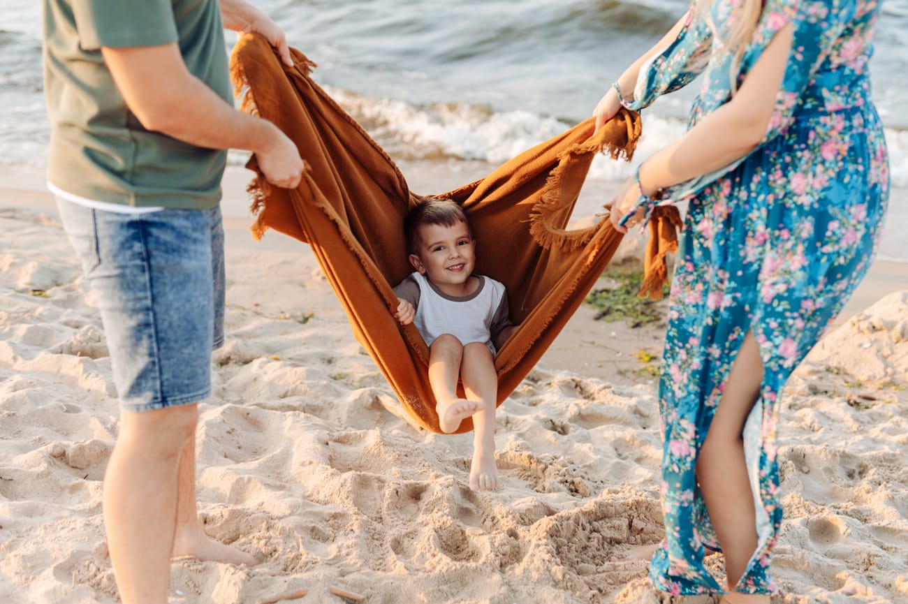 Chłopiec huśtany w kocu w trakcie nadmorskiej sesji o zachodzie słońca. 