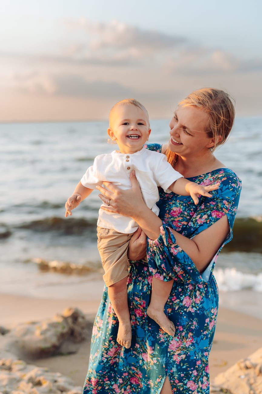 Mama trzymająca synka w ramionach o zachodzie słońca nad morzem. 